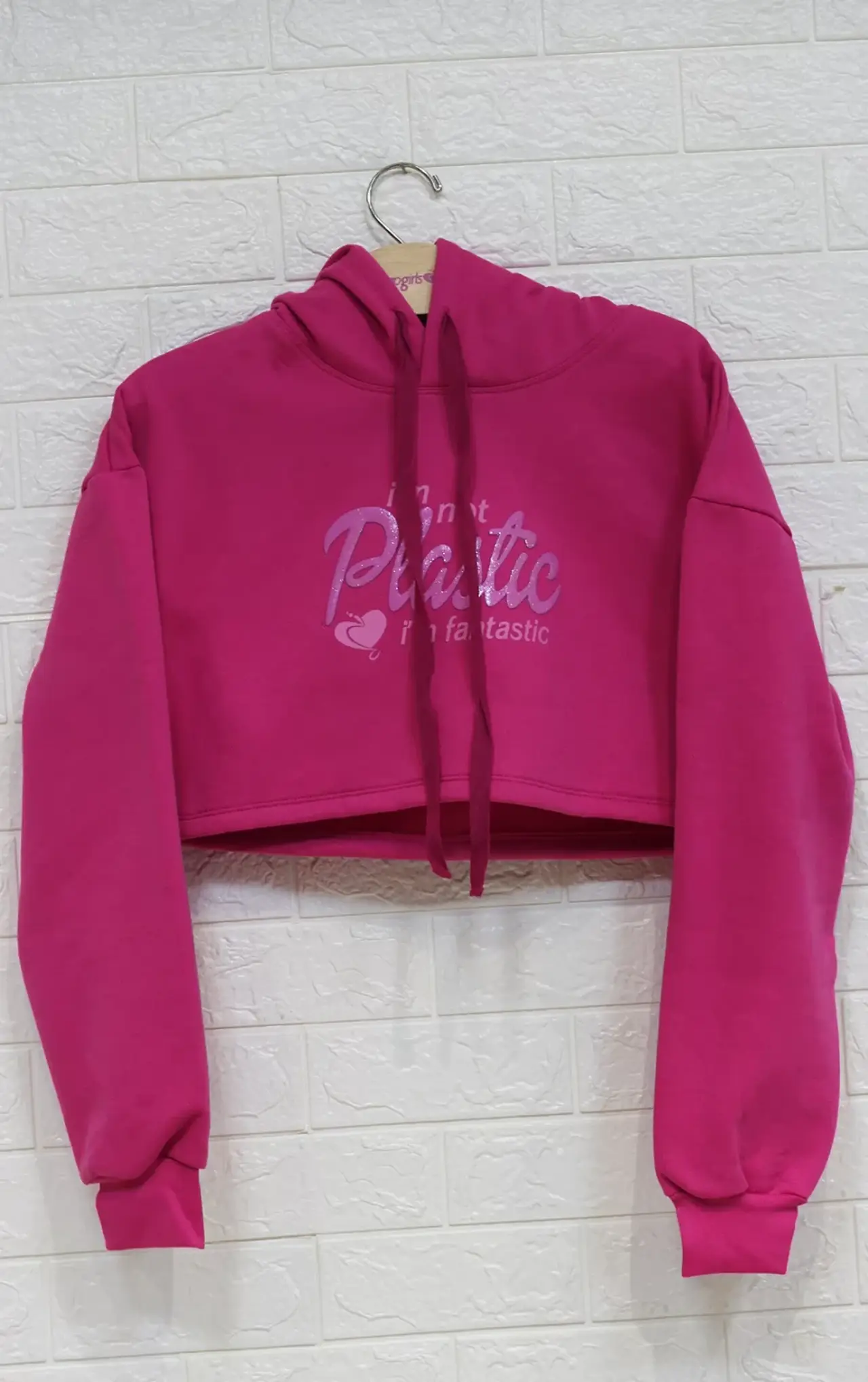 blusinha rosa pendurada em um cabide com fundo de tijolinho brancos