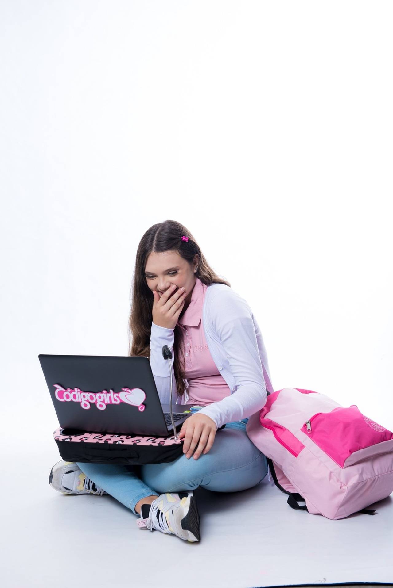 menina rindo de alguma coisa que está em seu computador sentada estudando em um espaço sozinha