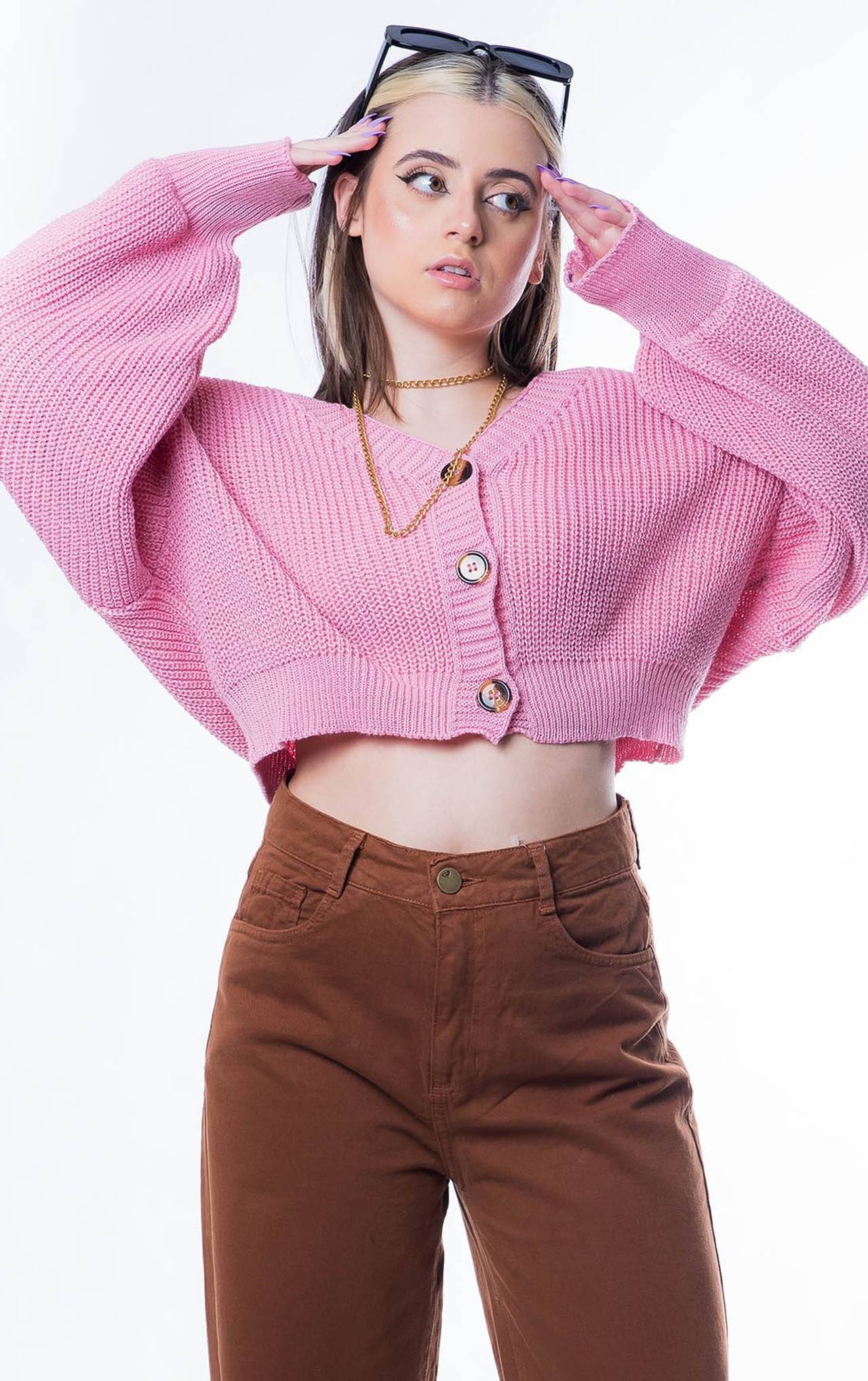 modelo posando com um tricot rosa e uma calça marrom