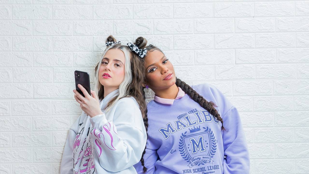 duas amigas encostadas na parede com o celular na mão