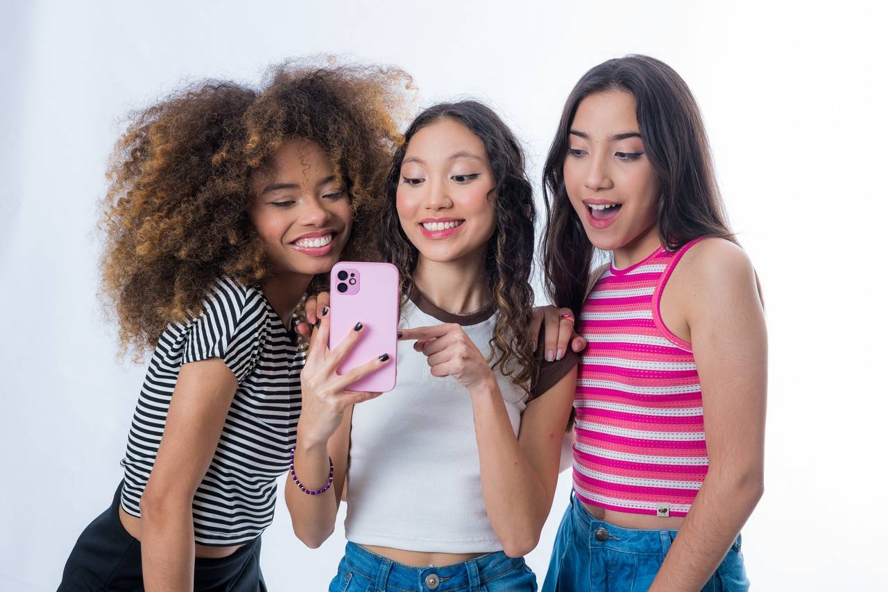 três meninas felizes mexendo no celular em uma festa do pijama